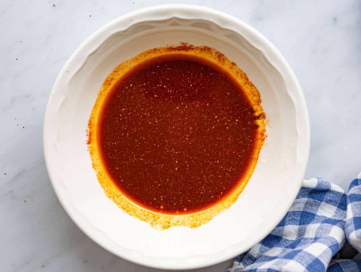Step 1 Mixing bowl with olive oil, lemon juice, garlic, and spices being whisked together.