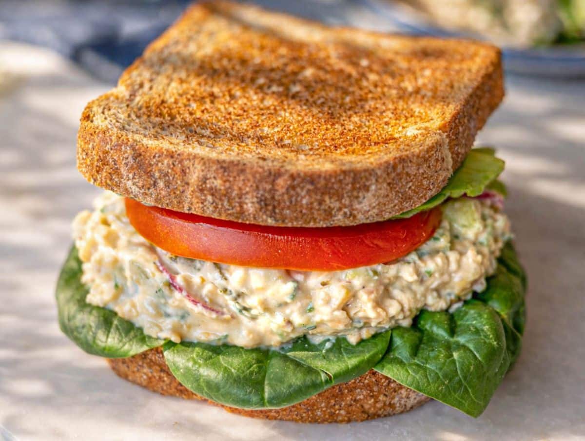 Thick chickpea salad sandwich on rustic bread, bright and inviting with fresh colors and texture.