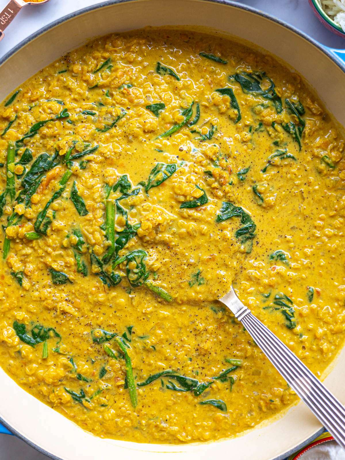 Top down of creamy red lentil dal showing soft lentils and spinach in a rich sauce.