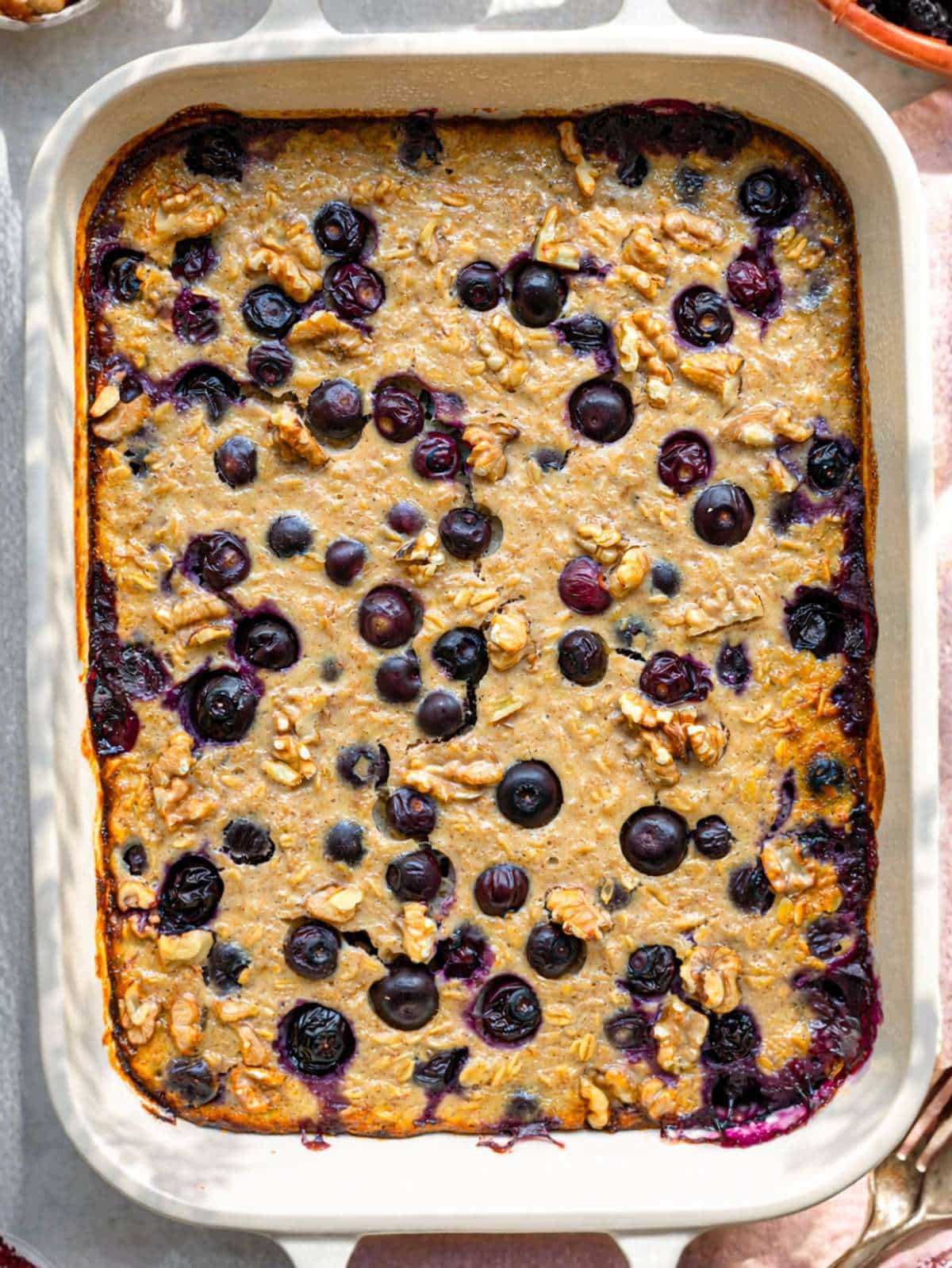 Baked blueberry baked oatmeal in ceramic dish with golden top and walnuts.