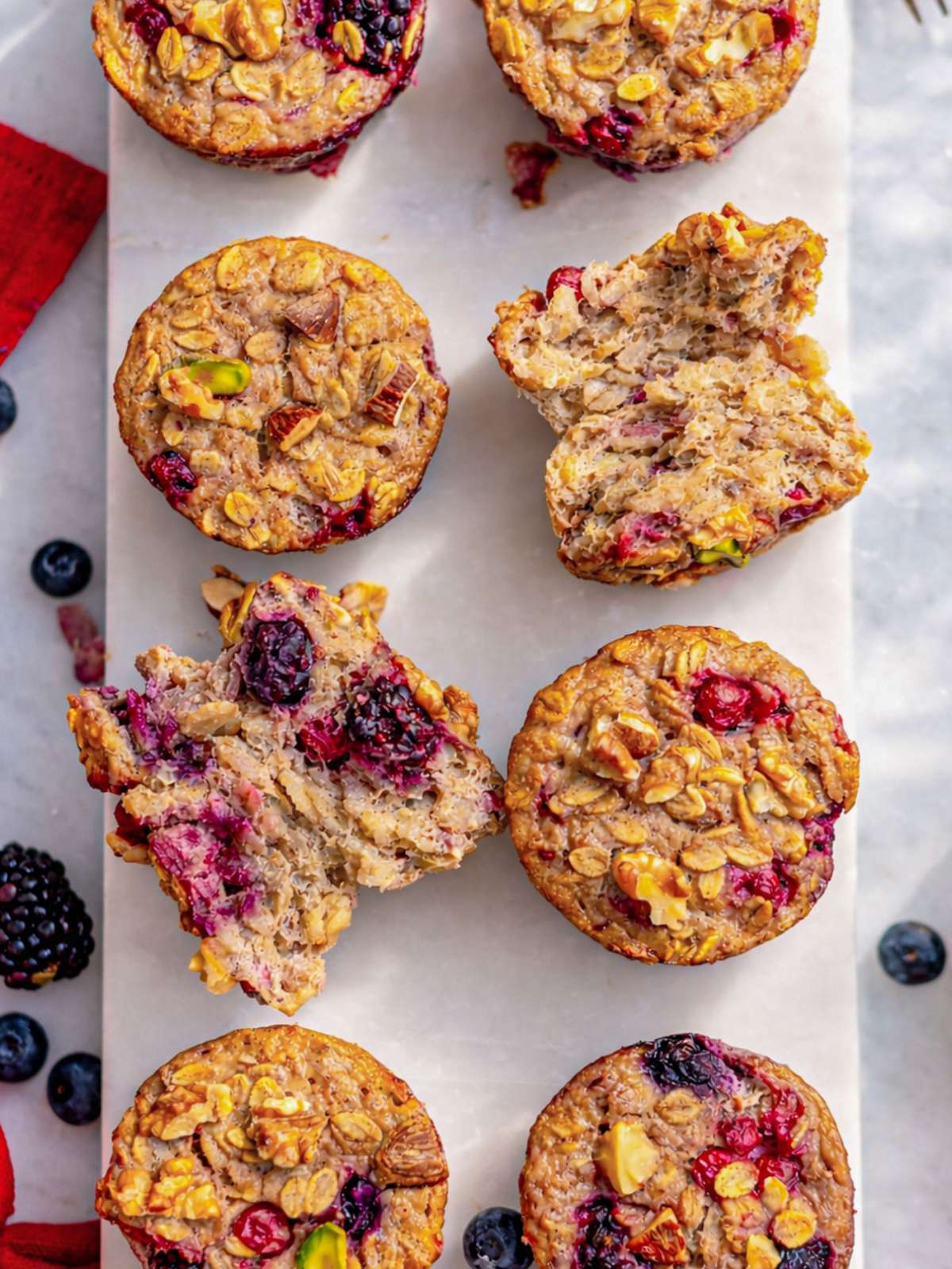 Baked oatmeal cups cooling on marble table with golden tops and berries.