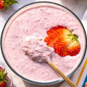Bowl of strawberry overnight oats on marble table near bright morning light.