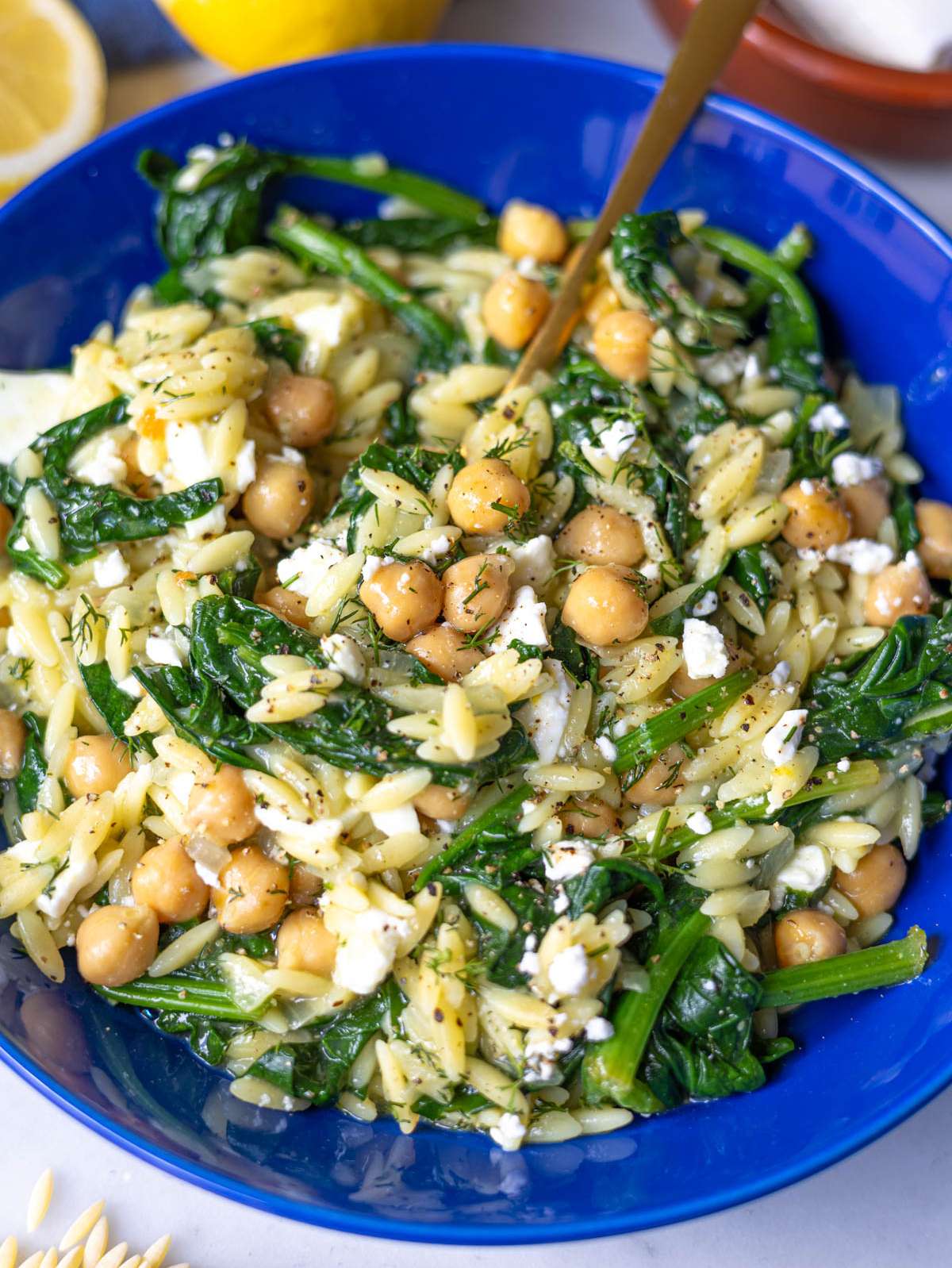 Close-up of creamy spinach orzo with chickpeas and crumbled feta in a bowl.