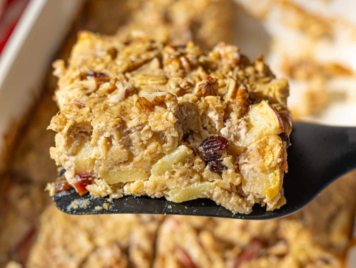 Close up slice of baked apple oatmeal lifted from dish with walnuts on top.