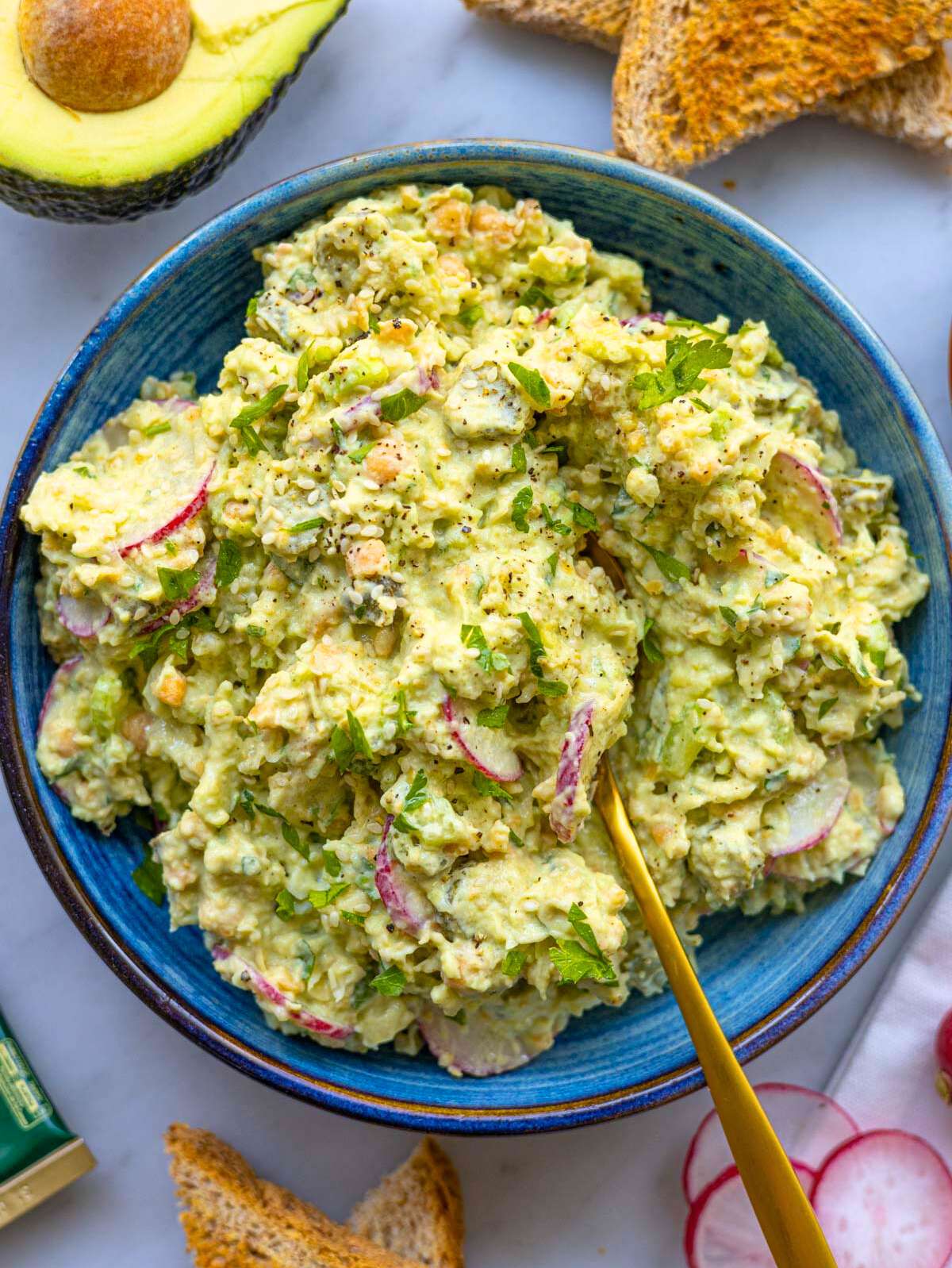 Creamy chickpea avocado salad served in a bowl with spoon and fresh herbs.
