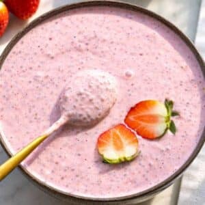 Creamy strawberry chia pudding in sunlight with spoon.