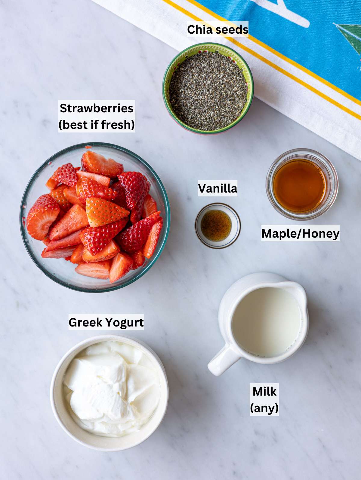 Fresh strawberries Greek yogurt chia seeds milk maple syrup vanilla arranged on kitchen counter.