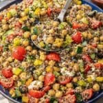 Greek quinoa salad served family-style on a large platter with fresh vegetables and feta visible.