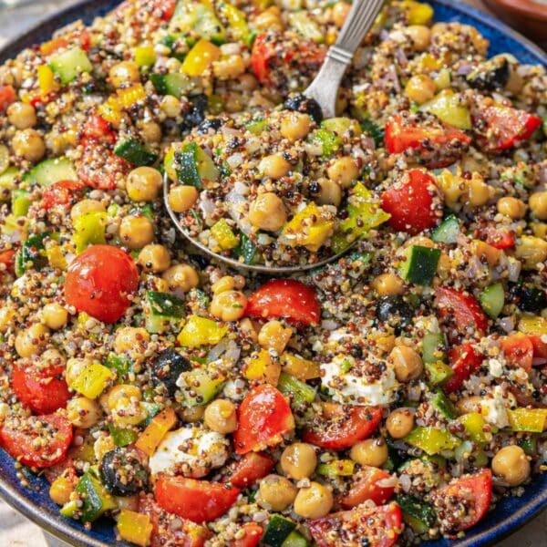 Greek quinoa salad served family-style on a large platter with fresh vegetables and feta visible.