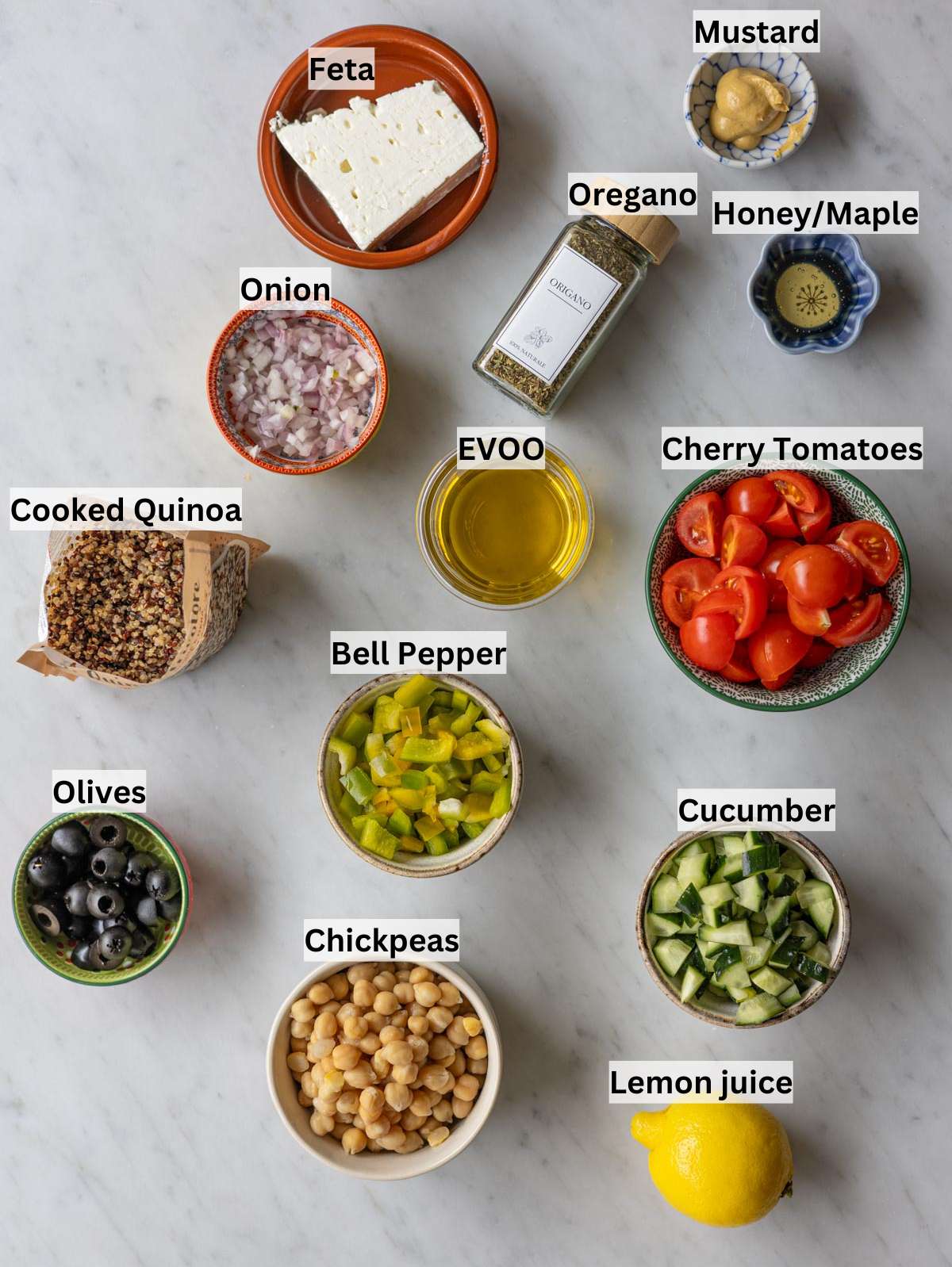Ingredients for Greek quinoa salad arranged on a table with fresh vegetables and feta.