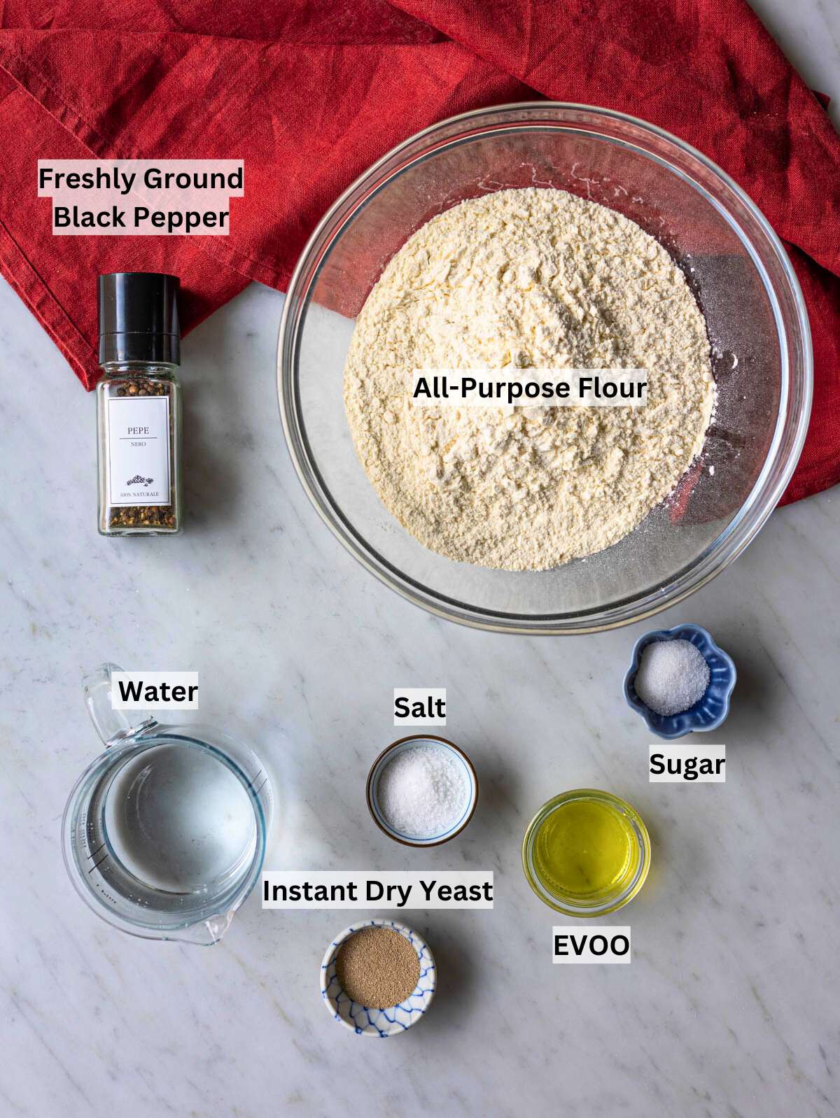Ingredients for black pepper focaccia including flour, olive oil, yeast, salt, and cracked black pepper.
