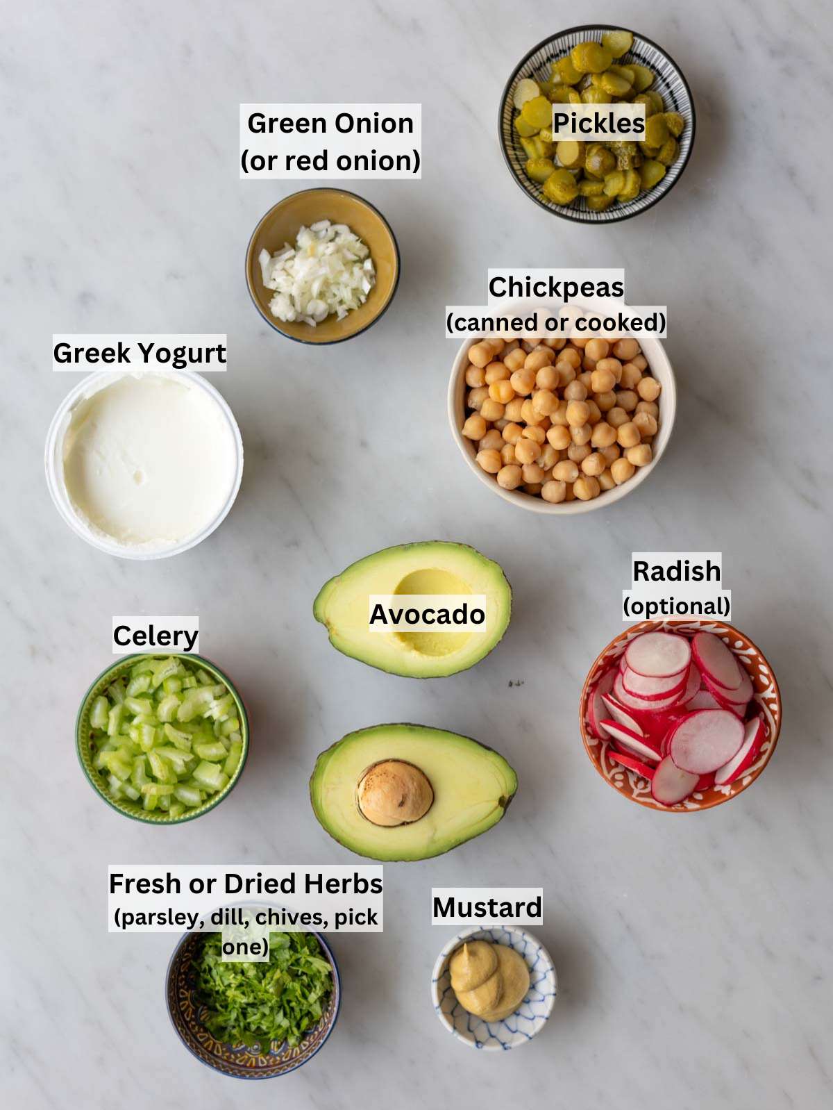 Ingredients for chickpea avocado salad arranged on a wooden table with fresh herbs and vegetables.