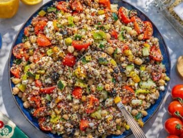 Mixed Greek quinoa salad with dressing evenly coating vegetables and grains.