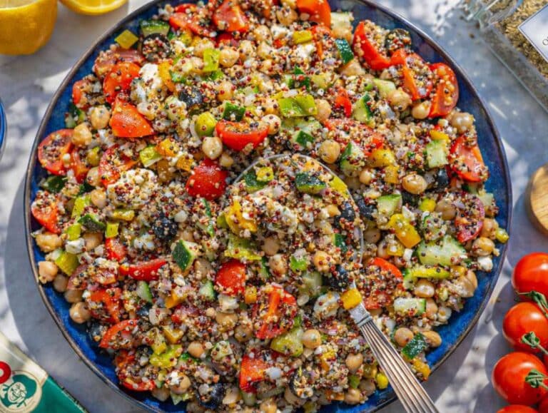 Mixed Greek quinoa salad with dressing evenly coating vegetables and grains.