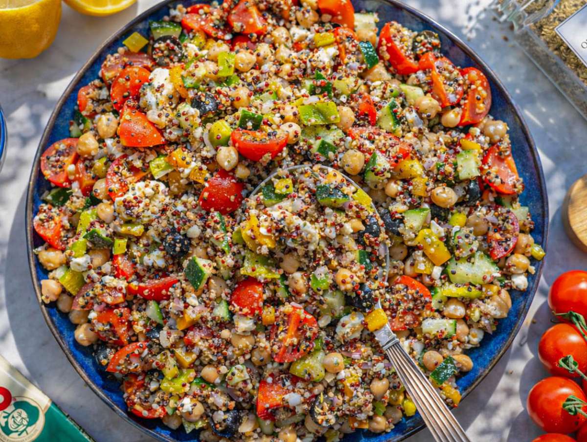 Mixed Greek quinoa salad with dressing evenly coating vegetables and grains.