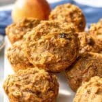 Morning glory muffins stacked high on table with visible oats and carrots.
