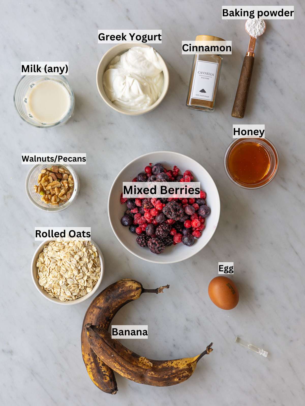Ripe bananas, oats, Greek yogurt, egg, honey, milk, and mixed berries on counter.