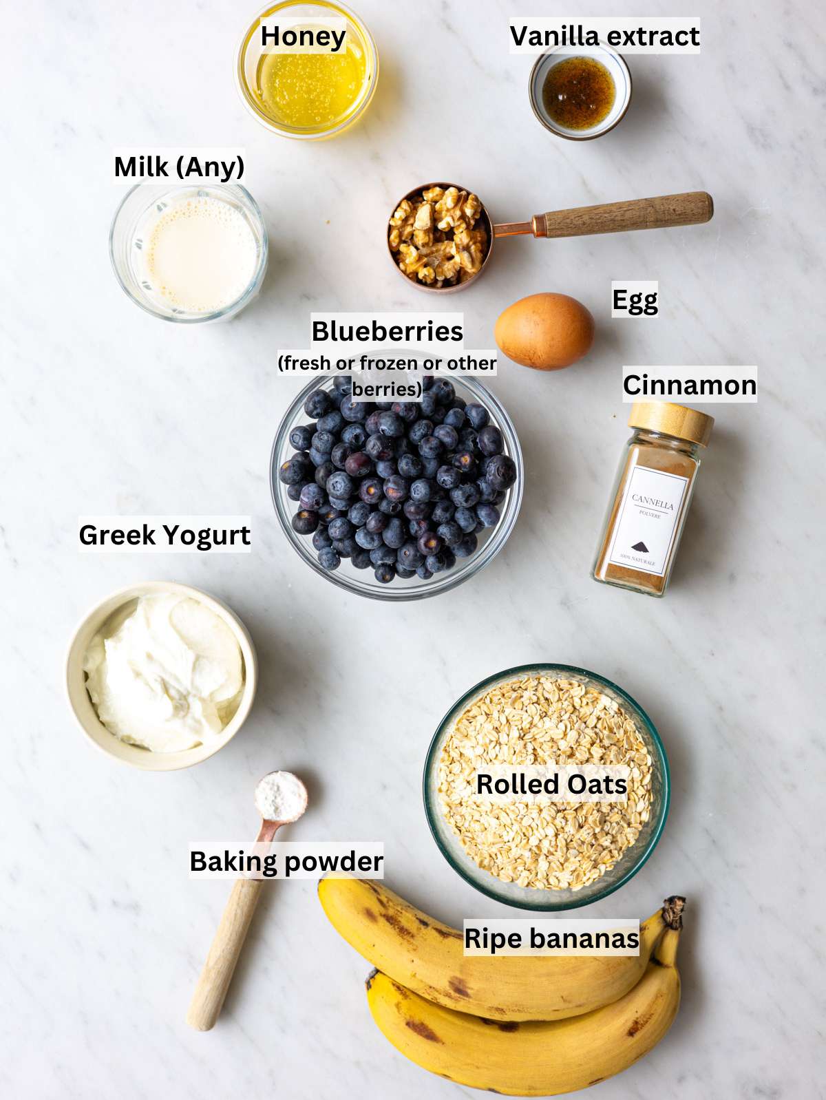 Ripe bananas, oats, blueberries, Greek yogurt, honey, egg, and walnuts on table.