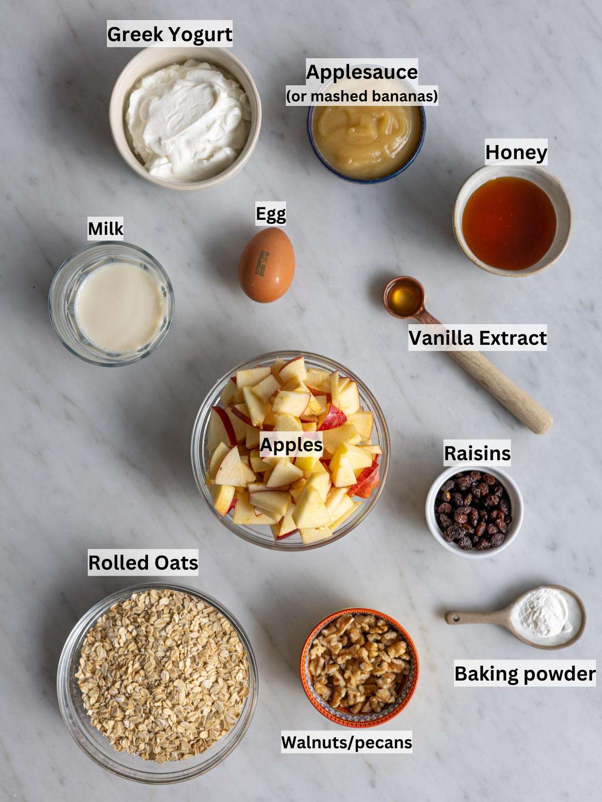 Rolled oats, apples, yogurt, milk, honey, egg, nuts, and cinnamon on table.