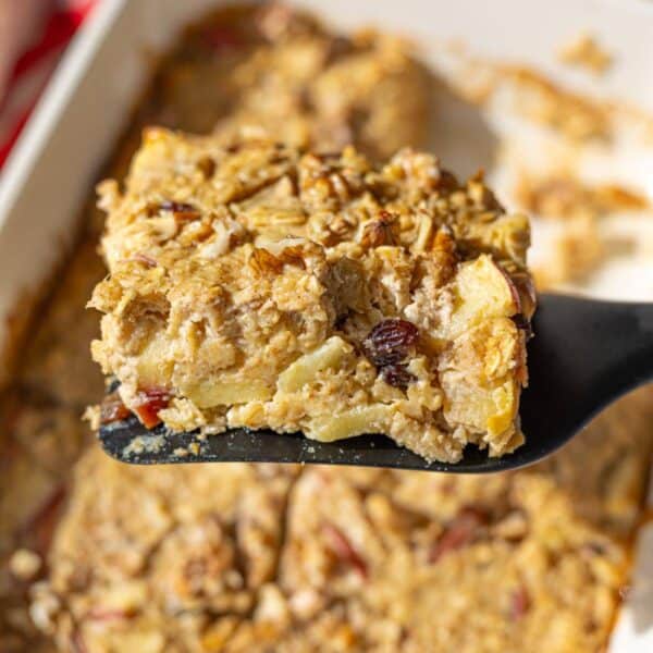Slice of baked apple oatmeal lifted from dish with walnuts on top.