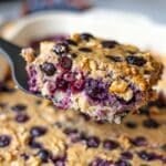 Slice of blueberry baked oatmeal lifted on spatula, juicy berries visible, pan below.