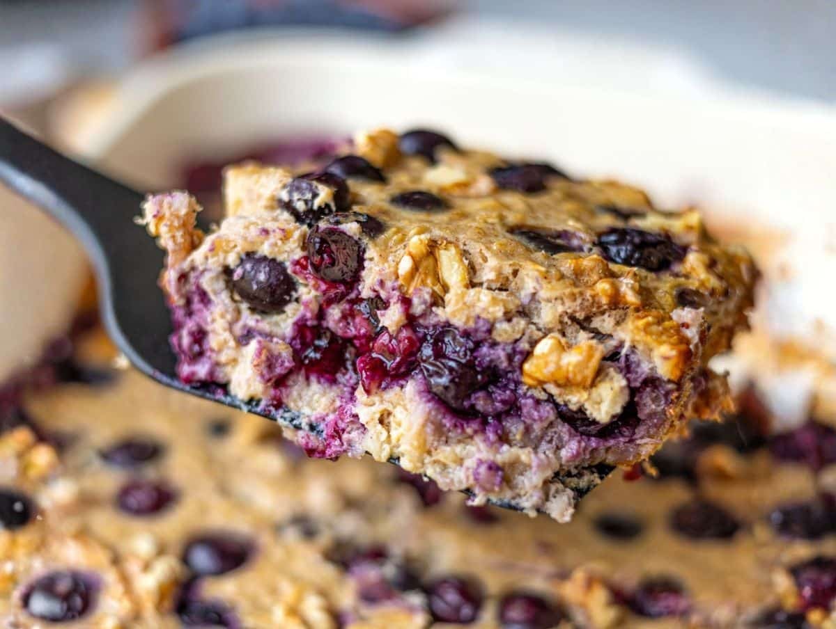 Slice of blueberry baked oatmeal lifted on spatula showing juicy blueberries.