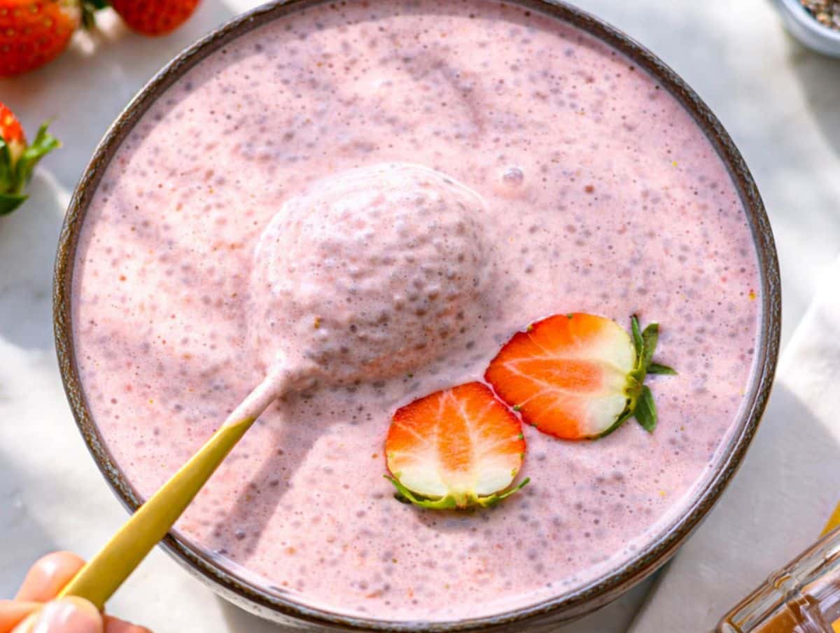 Soft pink strawberry chia pudding styled on breakfast table with fresh strawberries nearby.