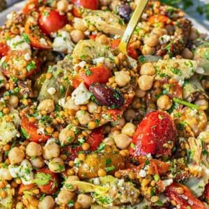 Spoon lifting colorful antipasto bean salad from large serving bowl.