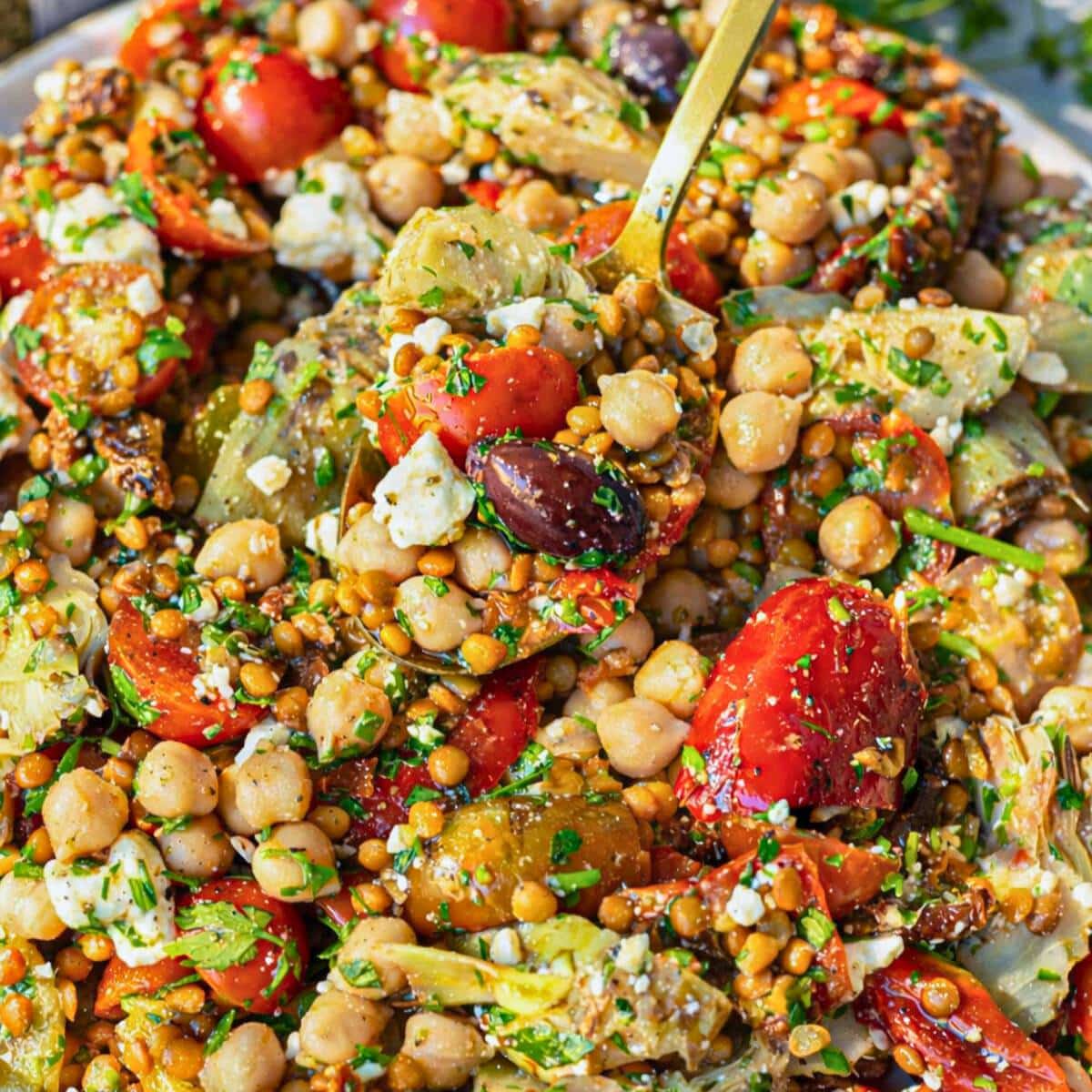 Spoon lifting colorful antipasto bean salad from large serving bowl.