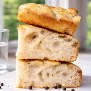 Stacked squares of black pepper focaccia on a marble surface by the window.