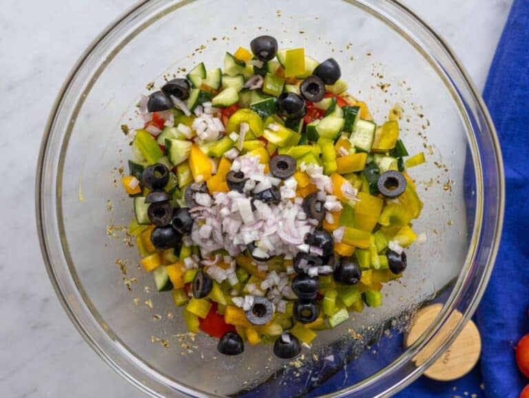 Step 3 Chopped cucumber tomatoes pepper onion and olives in the bowl with the dressing.