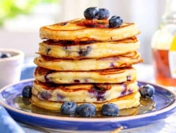 Step 4 Cooked pancakes stacked on a plate near sunlit window.