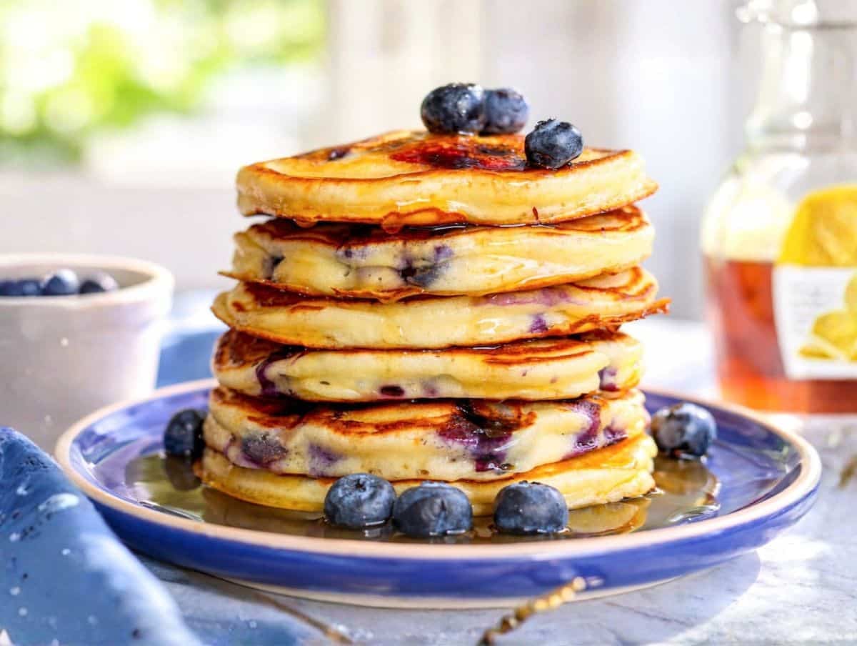 Thick Greek yogurt blueberry pancakes with syrup and bursting berries in soft morning light