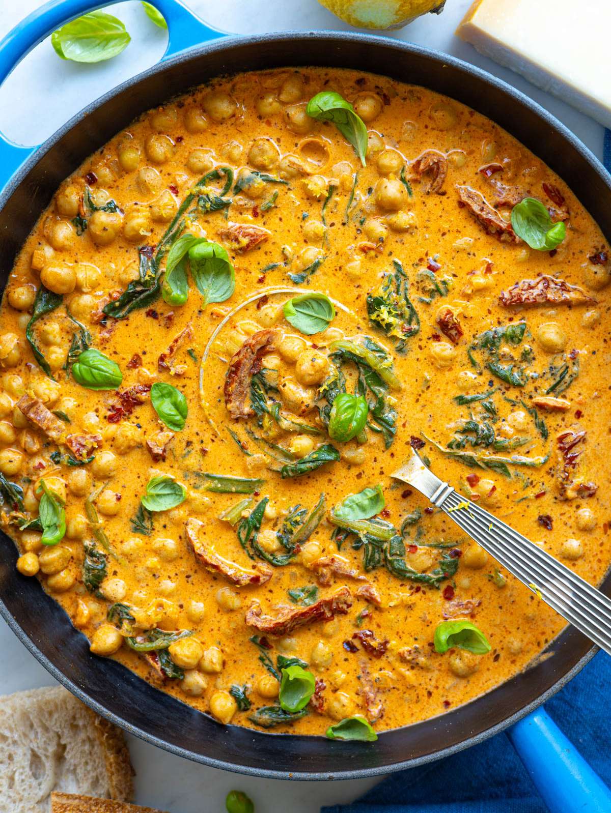 A creamy skillet of chickpeas and wilted spinach served on a white marble tabletop.