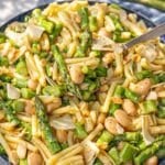 A large bowl of spring pasta salad next to a window with soft natural light.