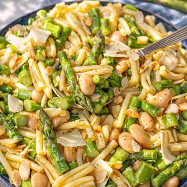 A large bowl of spring pasta salad next to a window with soft natural light.