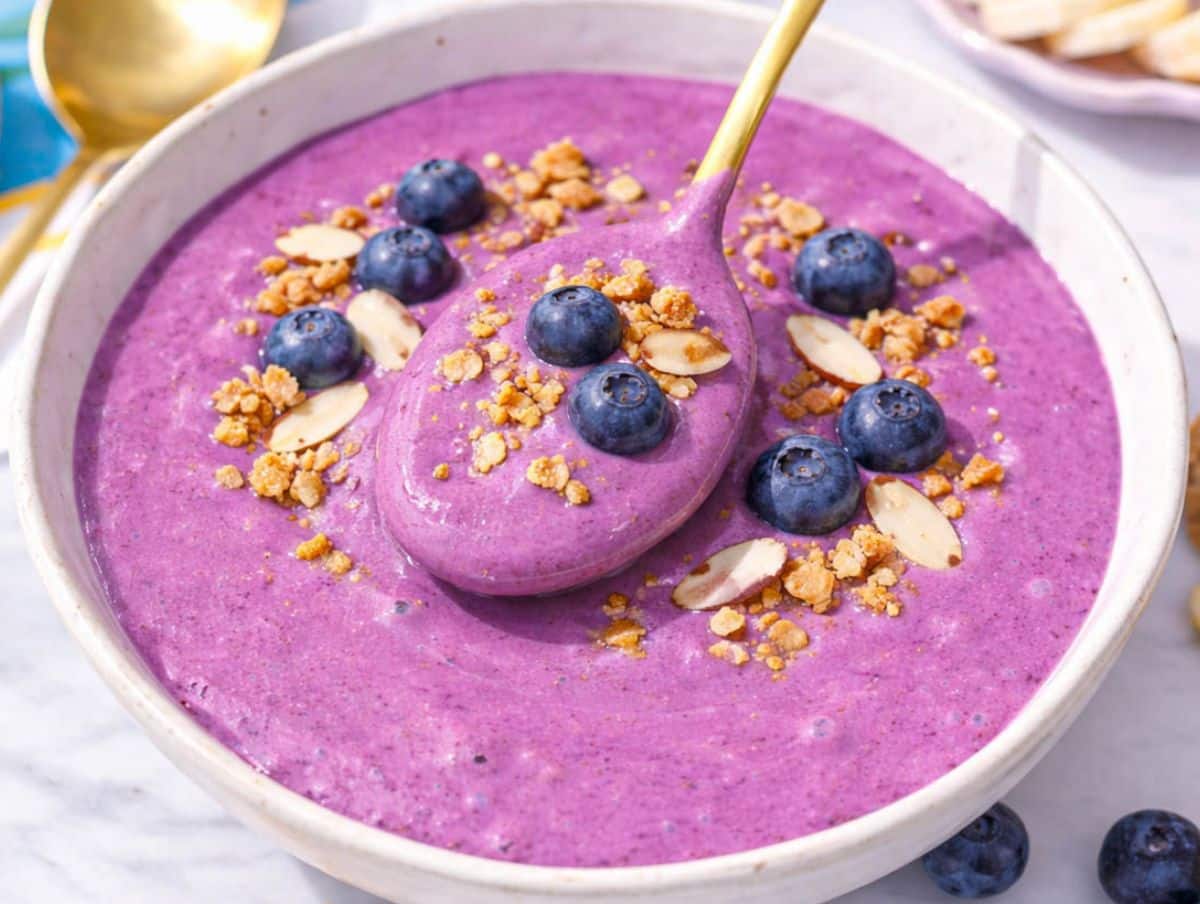 A refreshing breakfast scene with a spoon dipping into a thick and chilled blueberry smoothie bowl with Greek yogurt.
