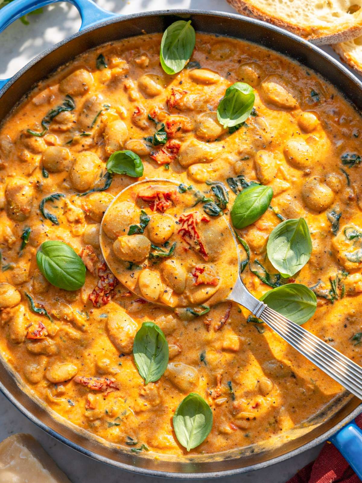 A skillet with Greek Yogurt Marry Me Butter Beans on marble next to crusty sourdough.