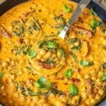 A vibrant bowl of Greek yogurt marry me chickpeas beside crusty bread on a marble surface.