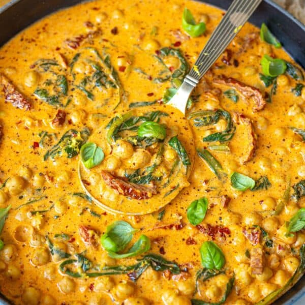 A vibrant bowl of Greek yogurt marry me chickpeas beside crusty bread on a marble surface.