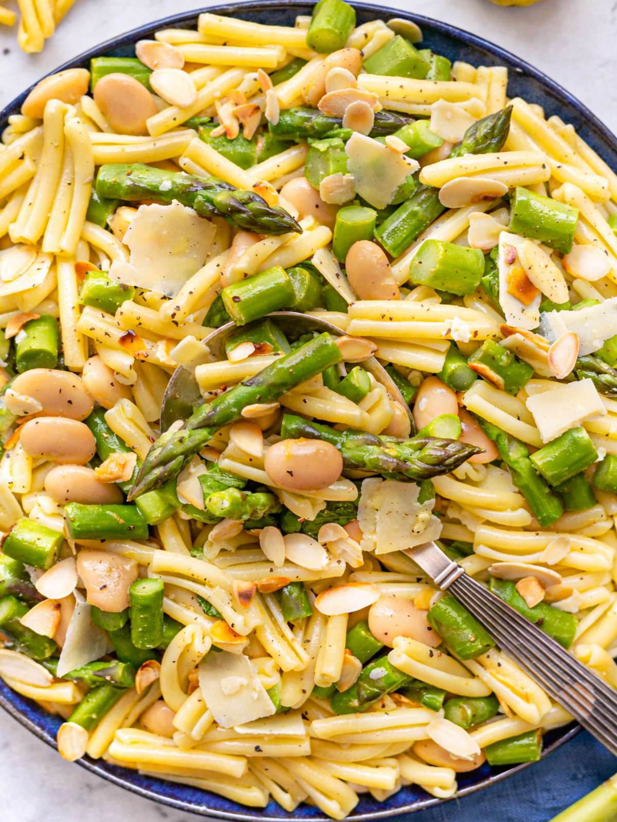 A vibrant lemon asparagus pasta salad in a ceramic bowl with shaved almonds and basil.