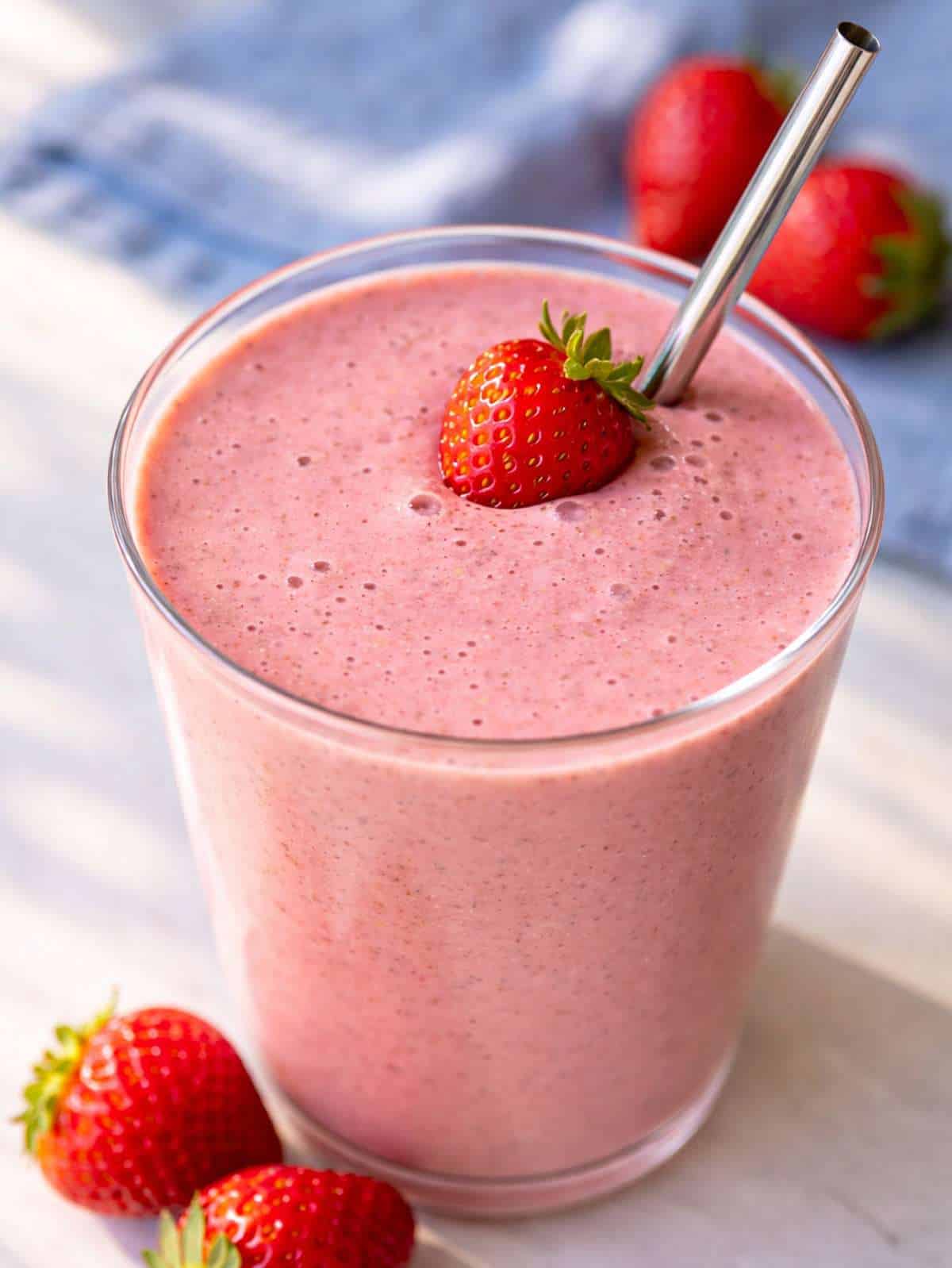 A vibrant strawberry smoothie with Greek yogurt in a glass with a fresh berry garnish.