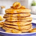 Banana oatmeal pancakes with Greek yogurt stacked on a plate near a bright kitchen window.