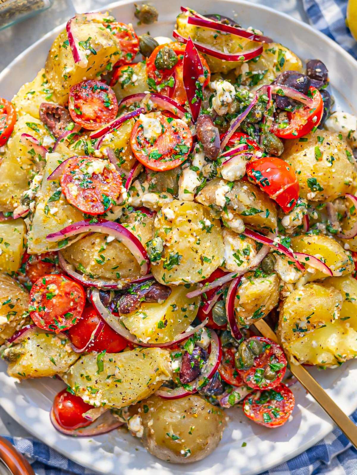 Bowl of Greek potato salad with tomatoes olives capers herbs and crumbled feta.