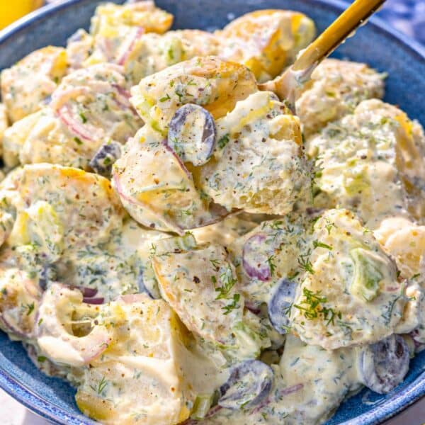 Bowl of Greek yogurt potato salad on marble table by bright window light.