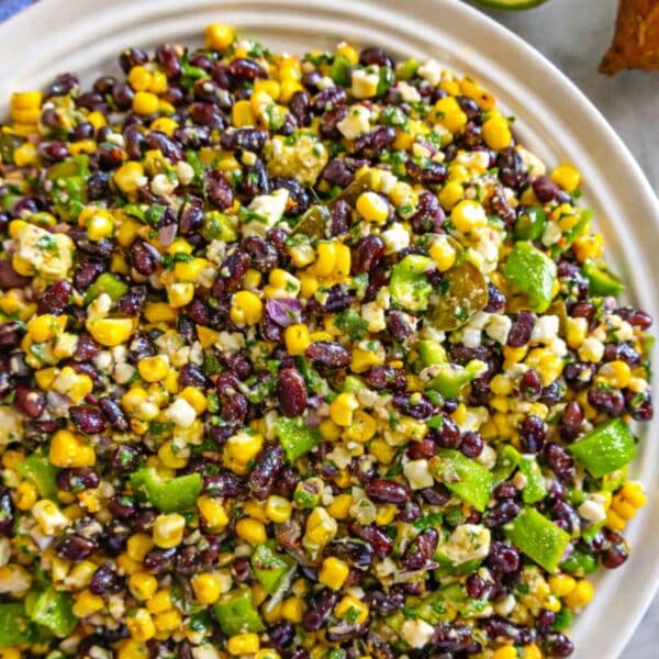 Bowl of chopped black bean salad with avocado corn and feta on bright marble table.