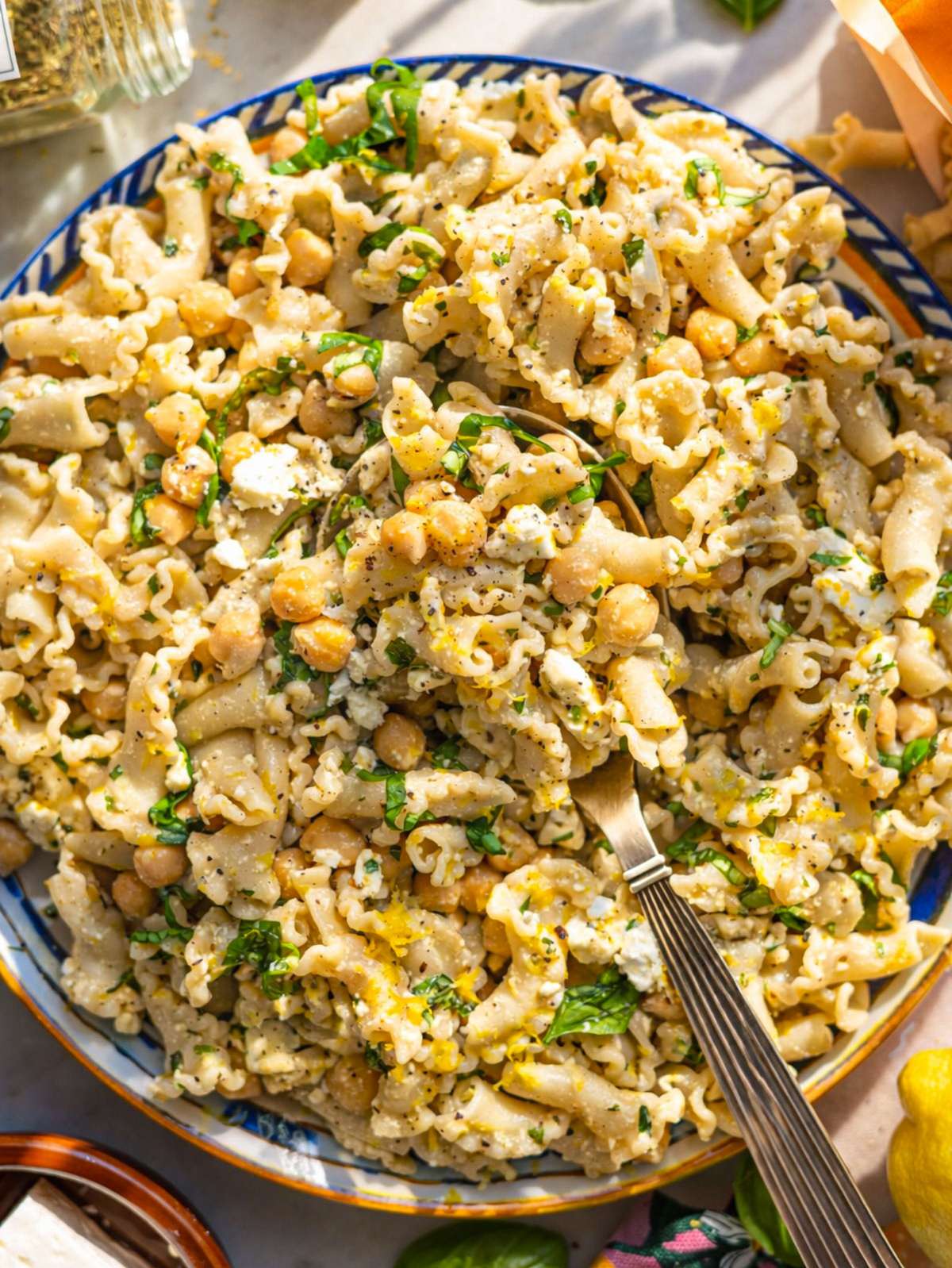 Bowl of lemon pasta salad with chickpeas herbs and feta on bright marble table.