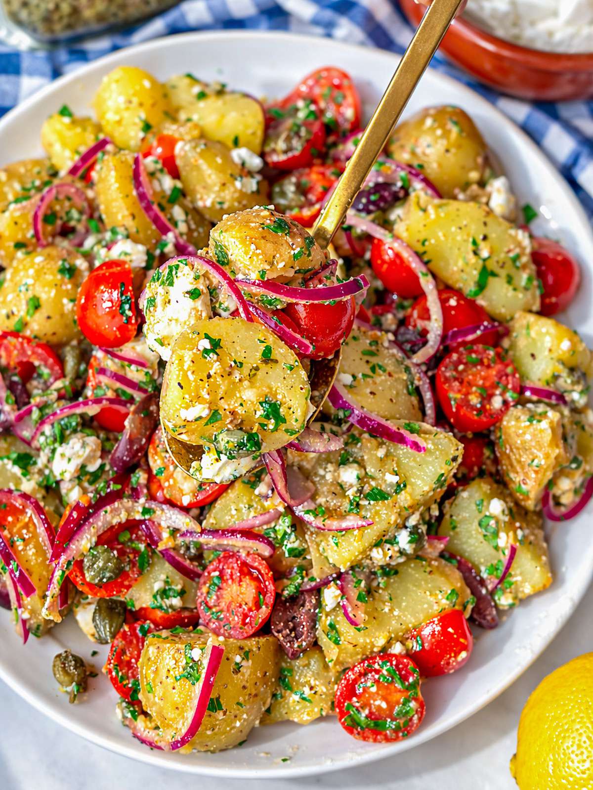 Close up of Greek potato salad showing tender potatoes feta olives and fresh herbs.
