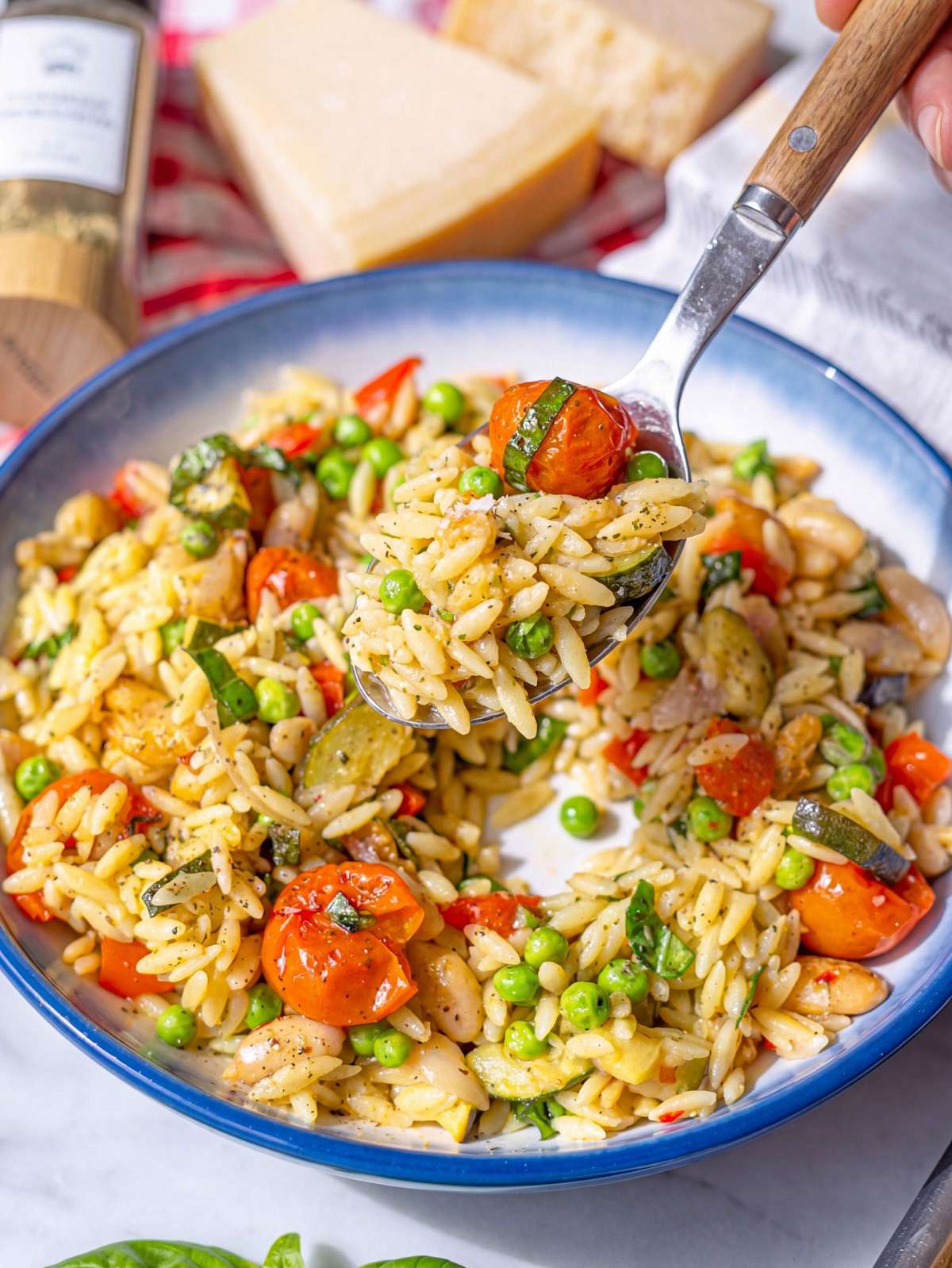 Close up of glossy orzo primavera with melted parmesan and roasted vegetables.