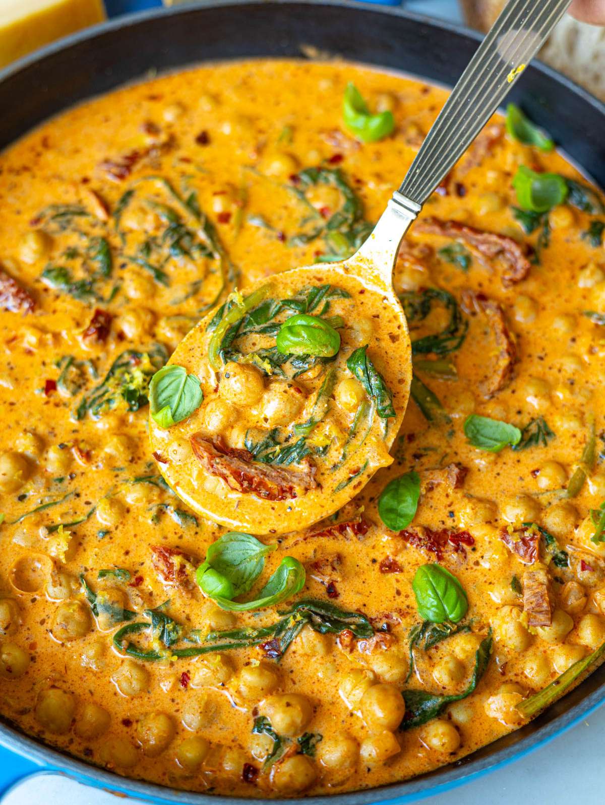 Close-up of tender chickpeas coated in a silky orange sauce with flecks of fresh basil.